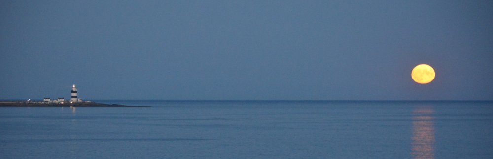 Views of the Hook Lighthouse and rising moon viewed from Dunmore East - near the start of the cliff walk. Co. Waterford, Ireland