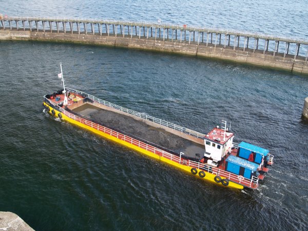 The dredger barge SANDSEND passing by the east pier wall of Whitby harbour.